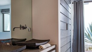 Une salle de bain moderne avec un grand miroir, un meuble-lavabo en bois foncé et une étagère intégrée où sont rangées les serviettes.