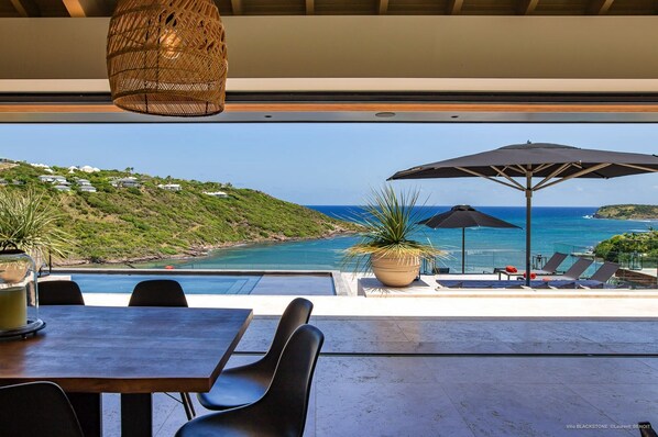 A poolside area with a view of the ocean, lounge chairs, and a table with chairs. - Villa BLACKSTONE – Secluded Luxury with Panoramic Ocean Views (Marigot)