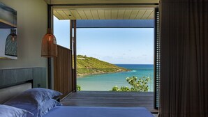 Een slaapkamer met een groot bed, uitzicht op de oceaan en een houten plafond.