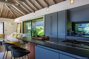 Une cuisine moderne dotée d’un grand îlot central, d’appareils électroménagers intégrés et offrant une vue sur la verdure.