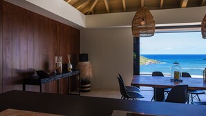 Een moderne eetruimte met uitzicht op de oceaan, houten lambrisering en hangende rieten lampen.