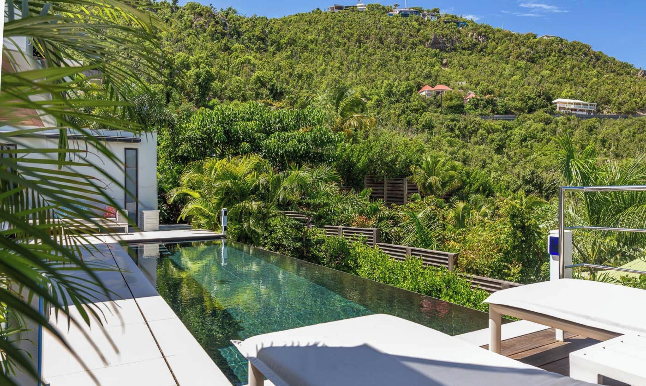 Un área junto a la piscina con sillones de descanso, una piscina cristalina y una exuberante ladera verde al fondo.