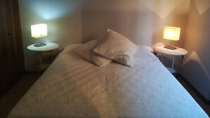 Un lit bien fait, recouvert d’une couette blanche à texture intéressante et agrémenté de deux oreillers, avec deux tables de chevet de chaque côté, sur lesquelles sont posées des lampes.