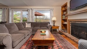 A living room with a sectional sofa, a wooden coffee table, a fireplace, and a large flat-screen TV. - Townhome with Fireplace & Hill Views, Saltbox (Hartford)