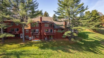 A multi-story red building with balconies, surrounded by trees and grass.