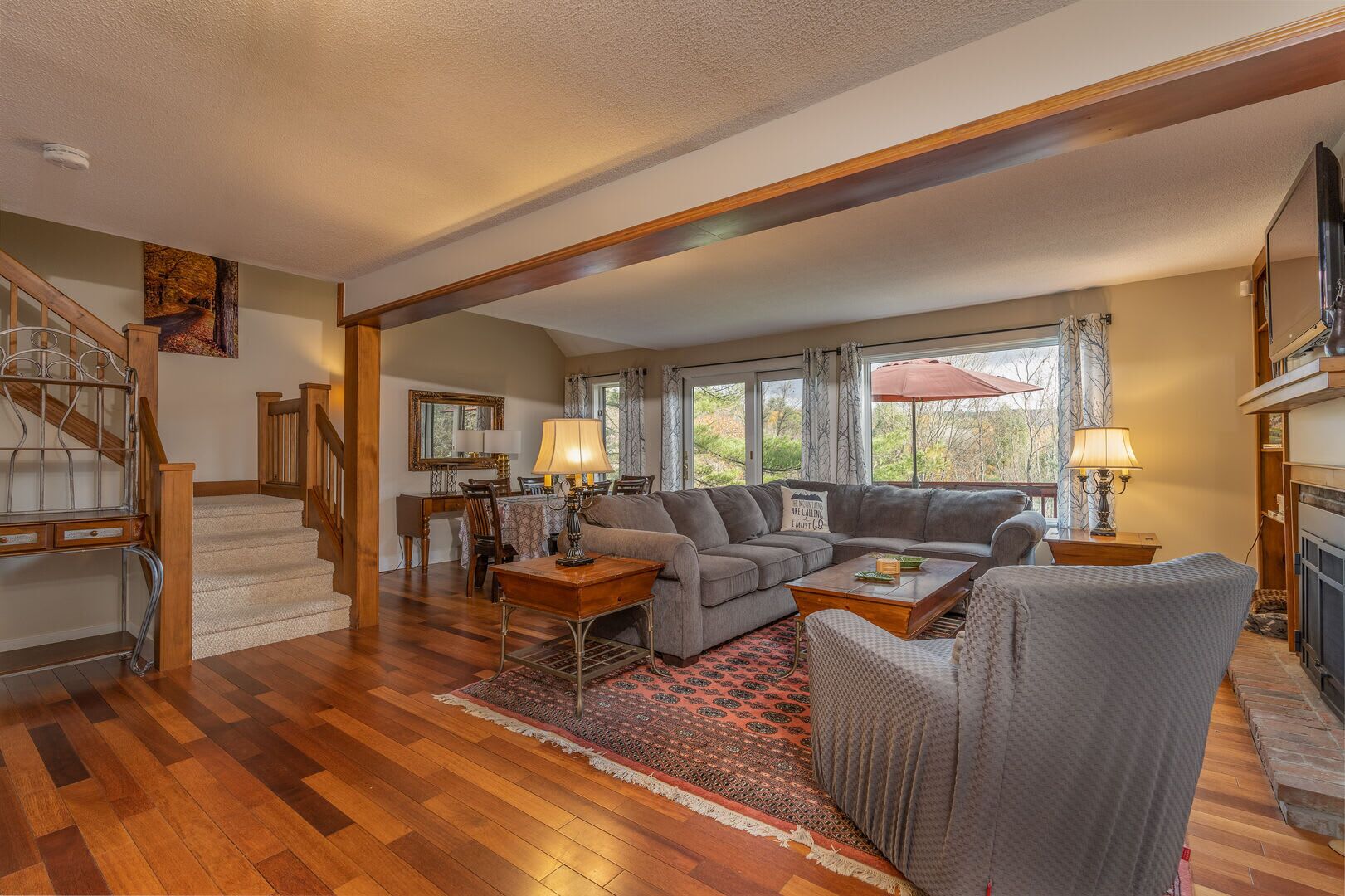 A spacious living room with a wooden staircase, a dining area, and a fireplace.