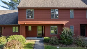 A two-story red building with a front porch, large windows, and a small front yard. - Townhome with Fireplace & Hill Views, Saltbox (Hartford)