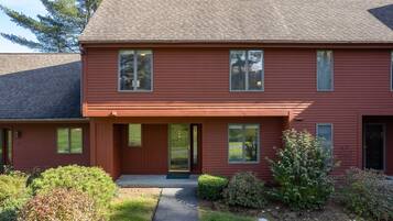 A two-story red building with a front porch, large windows, and a small front yard.