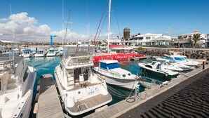 Un port esportiu amb diverses embarcacions amarrades, un edifici vermell destacat amb la senyalització 'Obycat.com' i una paret de pedra al fons.