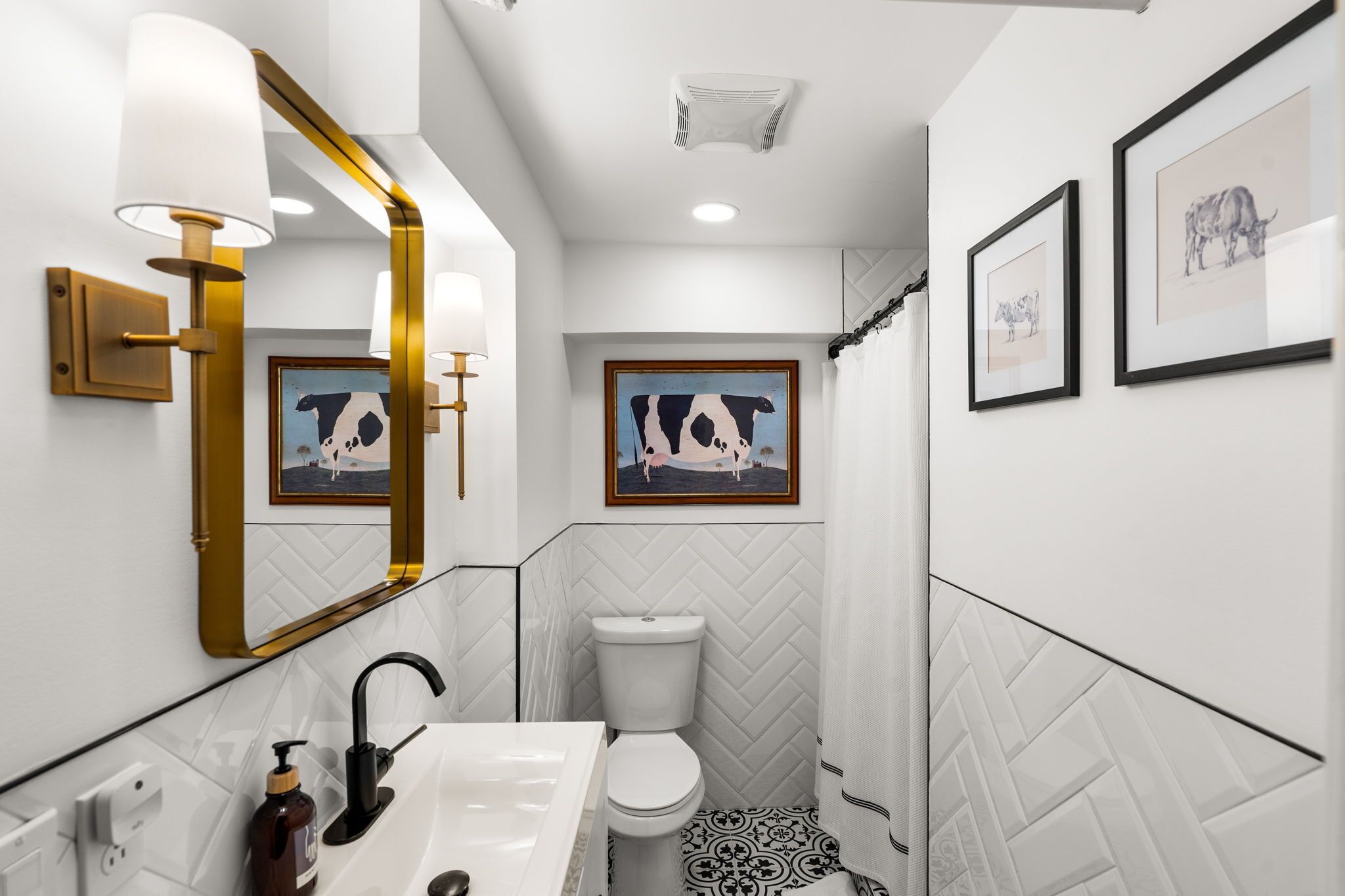 Une salle de bain avec un carrelage noir et blanc, des toilettes blanches, un lavabo blanc avec un robinet doré et un miroir avec un cadre doré.