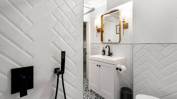 Un baño moderno con un patrón de baldosas en espiga, un lavamanos blanco con un espejo dorado y una estación de carga negra.