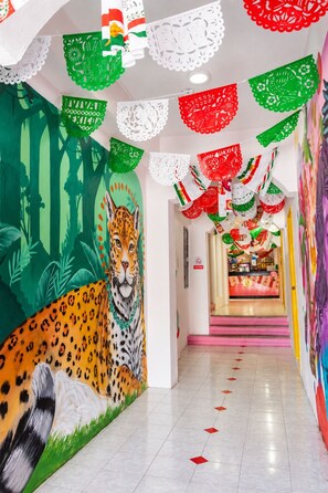 A hallway with a mural of a leopard, colorful paper decorations, and a brightly lit interior. - Rosa del Alba, Barrio Mágico Centro Histórico de Chetumal (Chetumal)
