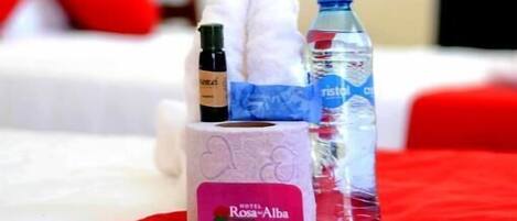 A hotel room with a bed, a red blanket, a bottle of water, a bottle of lotion, and a box of tissues.