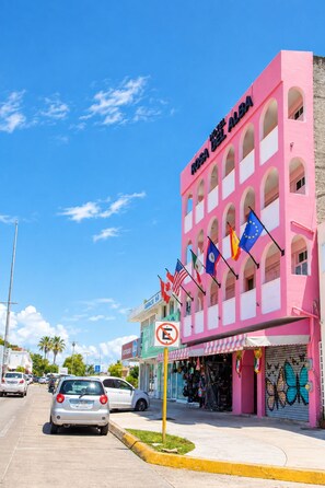Een roze gebouw met meerdere vlaggen, waaronder de Europese vlag, en een bord met de tekst 'Hotel Rosa Del Alba'.