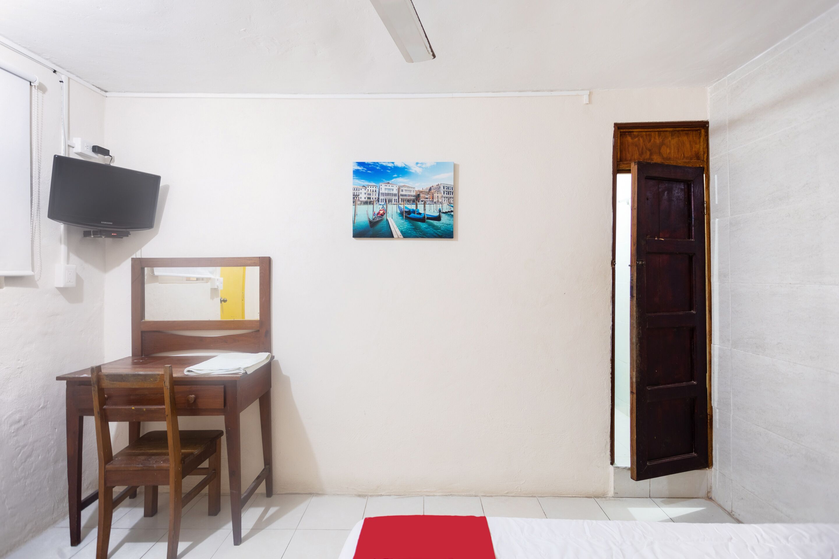 Una habitación con escritorio, silla, televisor y un cuadro que representa una escena de canal.
