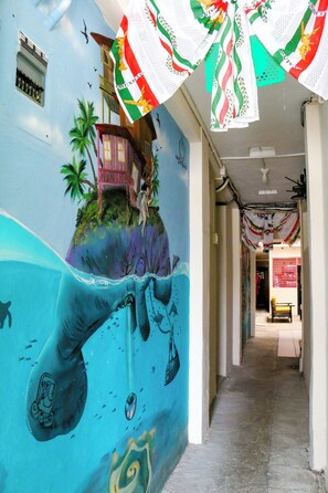 A mural with a hand holding a fishing rod on a blue wall, a small house on a cliff, and palm trees. - Rosa del Alba, Barrio Mágico Centro Histórico de Chetumal (Chetumal)