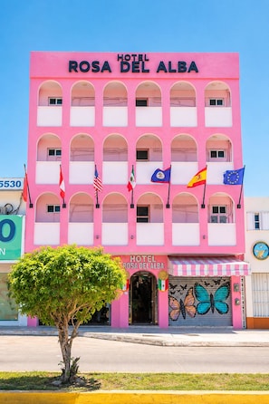 Un edificio rosa con el letrero 'Hotel Rosa Del Alba' y varias banderas.
