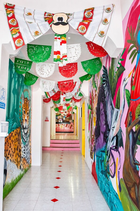 A hallway with colorful decorations, including paper cutouts and banners, leading to a brightly lit area with a counter. - Rosa del Alba, Barrio Mágico Centro Histórico de Chetumal (Chetumal)