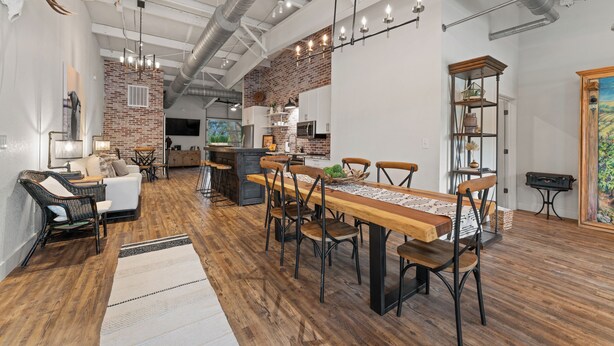 A spacious living area with a large wooden dining table, comfortable seating, a kitchen in the background, and exposed ductwork on the ceiling. - Entire Lodge (Bulverde)