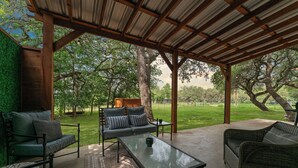 An outdoor patio with a covered seating area, a glass-top table, and a view of a grassy landscape. - Entire Lodge (Bulverde)
