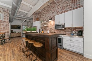 Una cocina con pared de ladrillo, armarios blancos, horno de acero inoxidable y una barra con taburetes.