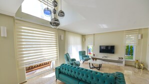 A spacious living room with a teal sofa, two armchairs, a coffee table, and a TV. - 4 bedroom luxury villa sardunya B in oludeniz fethiye (Fethiye)