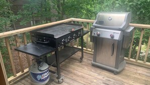 A barbecue grill and a propane tank on a wooden deck with a railing. - Tree house condo (Mt Ida)
