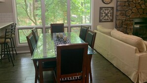 A dining area with a glass table, chairs, and a chandelier. There is a stone fireplace and a clock on the wall. - Tree house condo (Mt Ida)