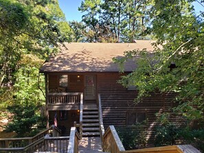 A log cabin with a wooden staircase leading to a porch, surrounded by dense trees. - Tree house condo (Mt Ida)