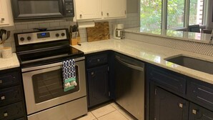A modern kitchen with white cabinetry, a black microwave, a stainless steel stove, and a dishwasher. - Tree house condo (Mt Ida)