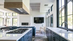 A modern kitchen with a central island, dark cabinetry, and large windows. - Modern Nordic Villa 3 miles from Beaver Stadium (State College)