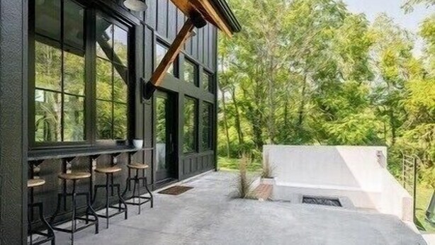 A modern outdoor bar area with a concrete floor, metal bar stools, and large windows overlooking a forested area. - Modern Nordic Villa 3 miles from Beaver Stadium (State College)