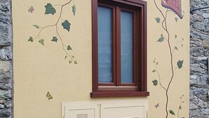 A building facade with a window and decorative vines. - Il Mondo In Valle (Pessinetto)