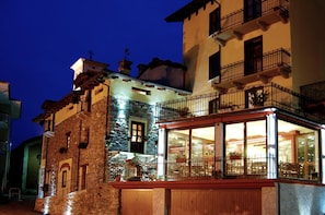 A building with a stone facade, a wooden balcony, and a glass-fronted shop or cafe. - Il Mondo In Valle (Pessinetto)