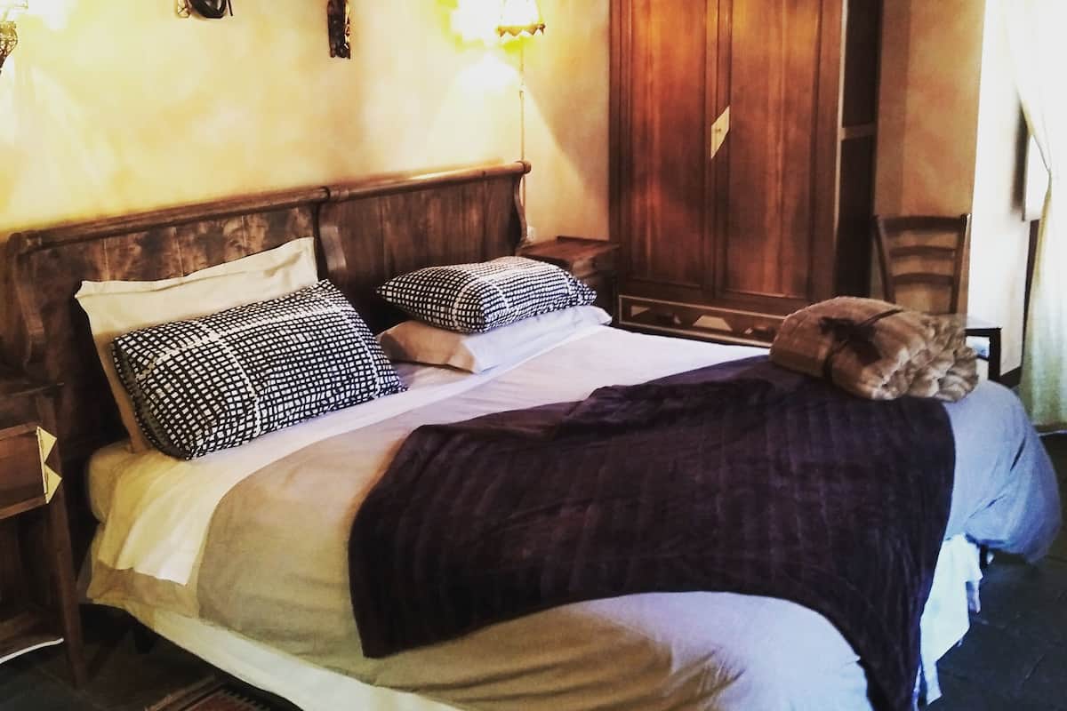A bed with a wooden headboard, two bedside tables, a nightstand, a wall-mounted light fixture, and a wardrobe.
