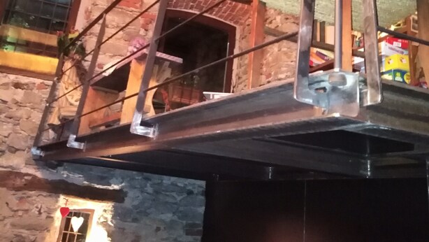 A rustic interior with exposed brick walls, a stone fireplace, and a metal balcony railing. - Il Mondo In Valle (Pessinetto)