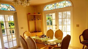 Un comedor con una mesa de vidrio y sillas de mimbre, un aparador de madera y vistas a través de una puerta con un vitral.