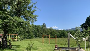 A grassy outdoor area with a swing set, a small garden, and a view of a forested area with mountains in the background. - Vacation in the countryside with mountain views and close to the Chiemsee (Frasdorf)