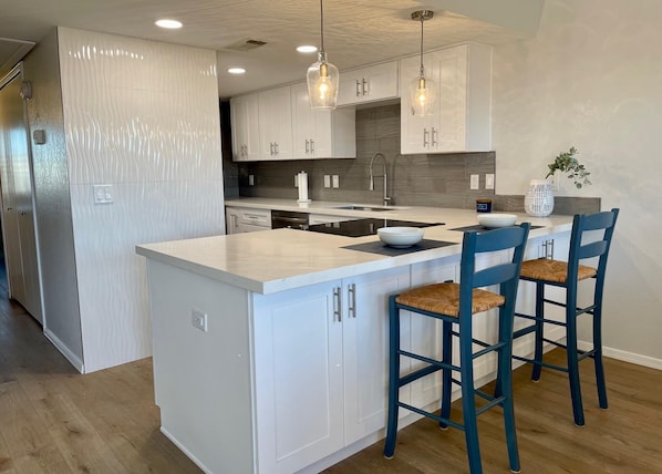 A modern kitchen with white cabinetry, a central island with bar stools, pendant lighting, and a backsplash.
