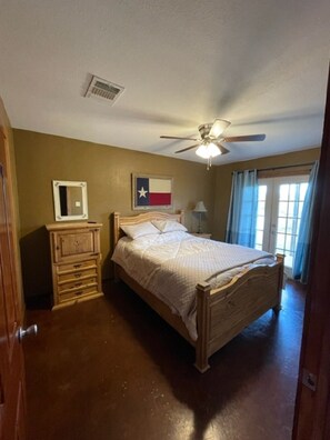 A bedroom with a wooden bed, a ceiling fan, a Texas flag on the wall, and a window with curtains.