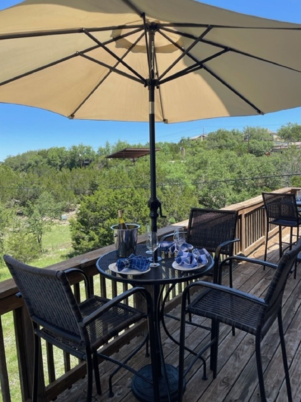 A deck with a table and chairs, a large umbrella, and a bottle of champagne.