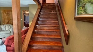 Un escalier en bois, doté d’une rampe, mène à un palier où se trouvent un canapé et un tableau.