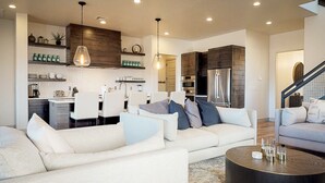 Un salon moderne avec un canapé, une table basse et un coin repas comprenant des chaises, et une cuisine en arrière-plan.