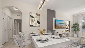 A modern dining area with a long table set for six, clear chairs, a chandelier, and artwork on the walls.