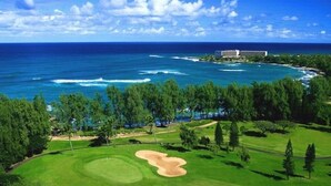 A golf course with a view of the ocean and a resort building in the background. - SeaHorseShort Term on Golf Course, Upper Floor - Have a relaxing vacation (Kahuku)