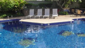 A swimming pool with clear blue water, lounge chairs, and a stone wall in the background. - SeaHorseShort Term on Golf Course, Upper Floor - Have a relaxing vacation (Kahuku)