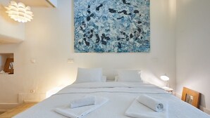 Ein Hotelzimmer mit einem großen Bett, weißer Bettwäsche, einem Gemälde an der Wand und einer modernen Leuchte.