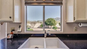 A kitchen with a double sink, a window with a view of a desert landscape, and a phone on the wall. - Unobstructed mountain views (Tucson)