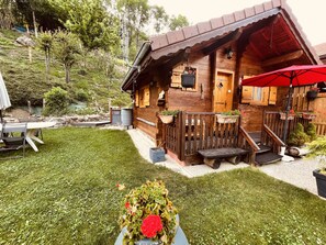 Una cabaña de madera con un porche, mobiliario exterior y un pequeño jardín.