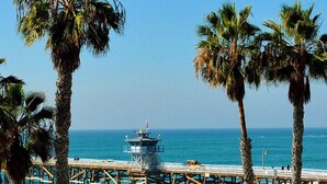 Ein Strand mit Palmen, einem Rettungsturm und einer Pier, die sich ins Meer erstreckt.